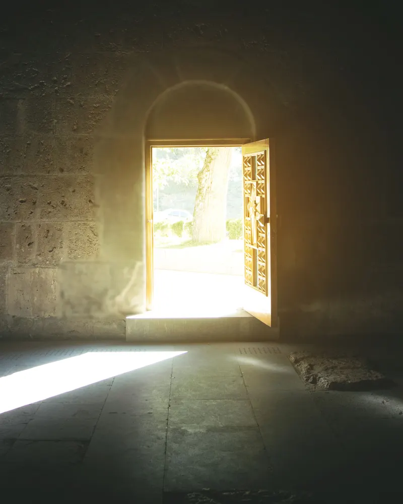 An arched doorway standing open, with daylight falling across a stone floor.